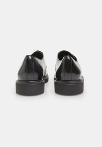 Chaussures en cuir noir avec un petit talon, texture lisse, forme arrondie et sans accents visibles. Le design comprend une vue arrière classique.