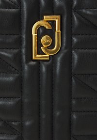 Sac à main en cuir noir avec texture matelassée, motifs de couture géométriques et un fermoir en métal doré affichant le logo.