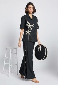 Maglietta nera a maniche corte con design di piante ricamato bianco, abbinata a pantaloni neri coordinati con fessure laterali e dettagli con bottoni.
