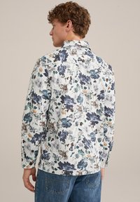 Chemise florale blanche avec des motifs bleus, verts et marron. Manches longues avec poignets à boutons, détail sur le dos, coupe décontractée.