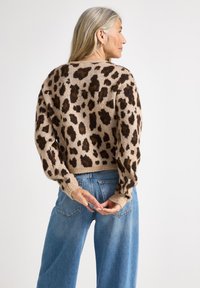 Pull en imprimé léopard beige clair avec des taches marron foncé. Matière en tricot douce, coupe décontractée, poignets côtelés, porté avec un jean taille haute.