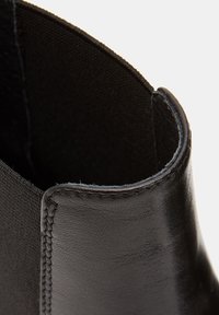 Crne kožne čizme do članka s glatkom površinom, elastičnom panelom i suptilnim detaljima šavova na otvaranju za članke. Minimalistički dizajn.