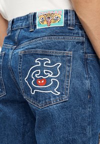 Τζιν παντελόνια με μπλε ξέπλυμα, με λευκή κεντημένη σχεδίαση στην πίσω τσέπη και πολύχρωμη ετικέτα ICECREAM στη μέση.