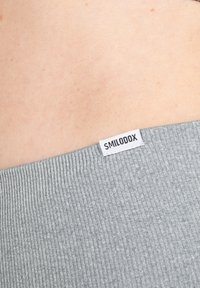 Grijze ribstof met een zichtbare witte label waarop "SMILODOX" is geborduurd aan de rand. De textuur lijkt zacht en elastisch te zijn.