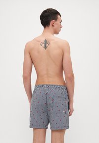 Bañador a rayas con acentos rojos. Cintura elástica, un bolsillo trasero, longitud a mitad del muslo. Fabricado en tejido ligero.