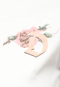 Στιλιζαρισμένο μπεζ γράμμα «D» που επικαλύπτει ένα ροζ τριαντάφυλλο με πράσινα φύλλα σε λευκό υφασμάτινο φόντο.