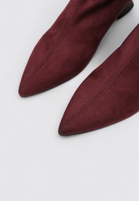 Botines de ante burdeos con puntera puntiaguda, con costuras visibles a lo largo de los lados y una textura mate suave.