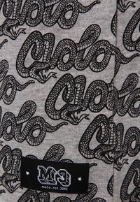 Šedá textilie s černými hadími grafikami propletenými s textem "Molo." Obsahuje černou etiketu se "M3" a "molo. est. 2003."