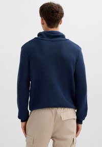 Suéter azul marino texturizado con cuello alto, mangas largas y puños acanalados, combinado con pantalones cargo beige.
