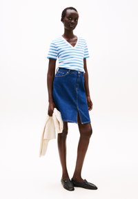 Stripete blå og hvit v-hals t-skjorte, denim blyantskjørt med splitt foran, holder en lett strikket genser, svarte slip-on loafers.