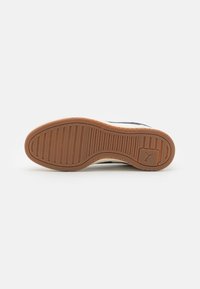 Semelle de basket avec bande de roulement en caoutchouc brun, rainures horizontales et verticales, et petit logo Puma près du talon.