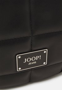 Borsa a tracolla nera trapuntata con una finitura testurizzata, dotata di una placca del marchio in metallo argentato che recita "JOOP! JEANS." Materiale liscio con cuciture a contrasto.