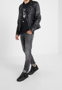 Chaqueta de motorista de cuero negra, camiseta gráfica negra, jeans de mezclilla grises, con puños enrollados, y zapatillas negras con detalles de cordones y suelas de goma.