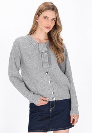 Cardigan grigio realizzato in morbido tessuto con colletto a coste e dettaglio con laccetto. Presenta bottoni silver e maniche lunghe, abbinato a una gonna in denim.