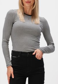 Haut à manches longues rayé noir et blanc, coupe ajustée, col rond, associé à un jean noir taille haute avec une étiquette de marque.