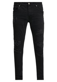 Pantalones vaqueros skinny negros hechos de denim, con acentos desgastados que presentan varios desgarros y bordes deshilachados. Bolsillos frontales y cierre de botón.