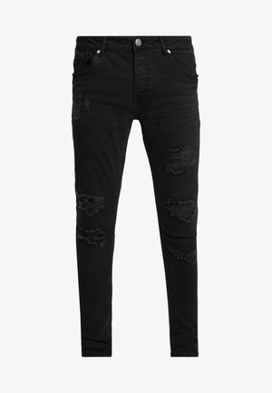 Pantalones vaqueros skinny negros hechos de denim, con acentos desgastados que presentan varios desgarros y bordes deshilachados. Bolsillos frontales y cierre de botón.