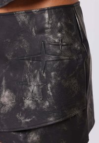 Jupe en cuir noir avec un motif texturé et usé, agrémentée d'accents métalliques. Formes d'étoiles en relief notables et ourlet lisse.
