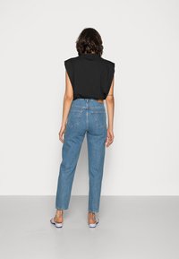 Top preto sem mangas, de corte descontraído; calças de ganga azuis de cintura alta com corte reto, com desgaste mínimo e detalhes discretos nos bolsos traseiros.