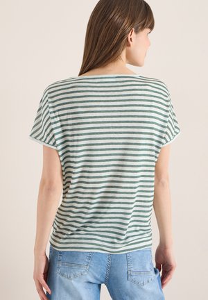 Femme portant un t-shirt à manches courtes à rayures horizontales blanches et vertes et un jean en denim bleu clair, vue de dos sur un fond uni.