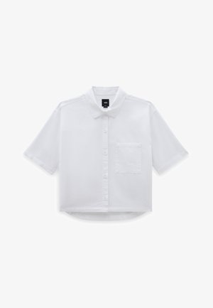 Camisa blanca de botones, falda maxi gris, pantalones anchos negros y zapatillas negras con cordones blancos, rematado con un gorro verde brillante.