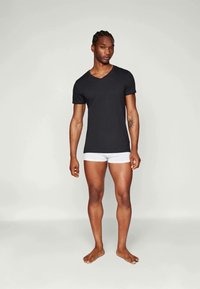 Black short-sleeve V-neck t-shirt, fitted design, worn with white boxer briefs. Smooth fabric, minimalistic style, model standing barefoot.