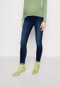 Graviditets mörkblå skinny jeans, stretchigt tyg. Matchad med grön ribbad toppen och ljusgröna anklarstövlar med spetsig tå och stilettklack.
