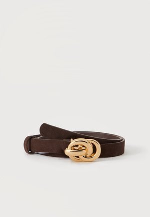 Ceinture en daim marron foncé avec une grande boucle dorée brillante entrelacée, roulée sur un fond uni clair.