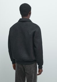 Giacca di misto lana grigio scuro con colletto, polsini e orlo a coste. Presenta una vestibilità rilassata e una trama liscia, vista da dietro.