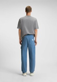 Grijze t-shirt met korte mouwen en blauwe cargo broek met meerdere zakken. De cargo broek heeft een patch label aan de achterkant aan de rechterkant. Witte sneakers.