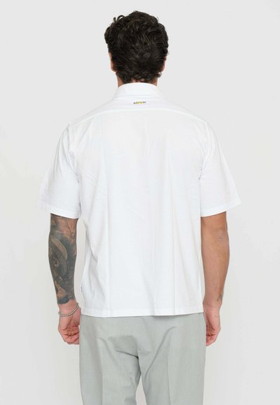 Camicia bianca a maniche corte con colletto e dettaglio del logo sul retro. Il tessuto appare liscio, con una vestibilità rilassata e orlo dritto.