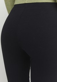Fekete bordázott leggings, szorosabb fazonnal, magas derékkal és olyan textúrával, amely kiemeli a bordázott mintát.
