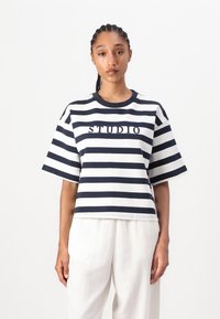 Marineblå og hvid stribet bomulds T-shirt med rund hals, korte ærmer og "STUDIO" broderet på forsiden. Boxy fit.