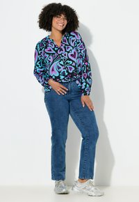 Blusa a maniche lunghe colorata con motivi a cuori viola e verde acqua su sfondo nero. Abbinata a jeans blu a vita media e sneakers argento.