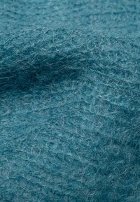 Turkusowy wełniany materiał o teksturowanej powierzchni i widocznych włóknach, tworzący miękki, ciepły wygląd.