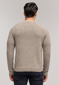 Beżowy sweter dziany z okrągłym dekoltem, ściągaczami u dołu i na mankietach, z teksturowanym wzorem i luźnym krojem. Noszony z ciemnymi dżinsami.