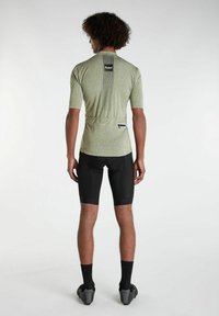 Zelený cyklistický dres s krátkym rukávom a vertikálnym prúžkovým dizajnom na chrbte, skombinovaný s čiernymi cyklistickými šortkami a čiernymi ponožkami.