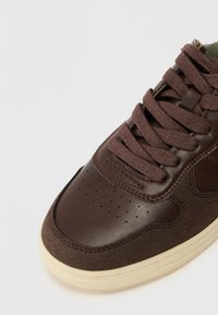 Sneaker in pelle marrone con accenti in suede testurizzato, punta rotonda, dettagli perforati, lacci marroni e suola in gomma color crema.