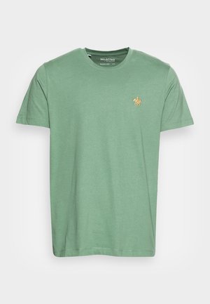 Žalias medvilninis marškinėliai su apvalia iškirpte, trumpomis rankovėmis ir mažuoju oranžiniu logotipu ant krūtinės. Lygus audinys, laisvas siluetas.