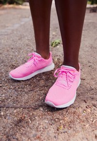 Bright pink athletic shoes with mesh material, white accents, and laces. Smooth sole, minimalistic design, suitable for sports or casual wear.