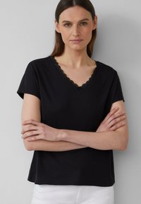 Top noir à manches courtes avec un décolleté en V orné de dentelle. Matériel doux avec une coupe décontractée, ourlet droit et détails minimaux.