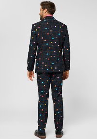 Black suit with a colorful retro game pattern featuring ghosts and maze lines, made from smooth fabric. Includes matching pants and a pink shirt.