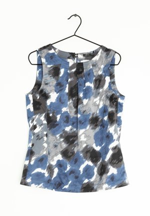 Blouse sans manches avec motif abstrait bleu, noir, gris et blanc suspendue sur un cintre noir sur fond blanc.