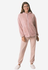 Lyserød, fluffy zip-up hættetrøje med hætte og to frontlommer, matchet med bløde lyserøde joggers og hvide teksturerede hjemmesko.