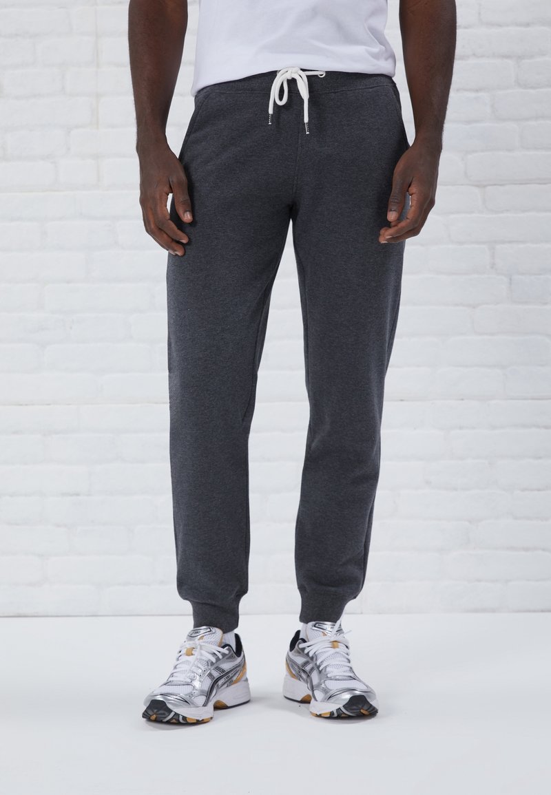 Grå atletiska joggingbyxor i mjukt material, med resårmidja och snörning samt avsmalnande ben. Bärs med silverfärgade löparskor.