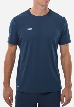 Mann trägt ein marineblaues, kurzärmeliges Sportshirt von Millet mit strukturiertem Stoff und kleinem Logo auf der Brust und am unteren Saum.