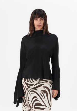 Black long-sleeve top with a high neckline, smooth texture, and flared cuffs, paired with a patterned brown and white skirt.