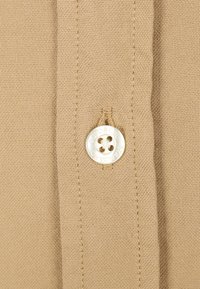Beige stof met een gestructureerde weving en een prominente witte knop waarvan "COLORFUL" is gegraveerd, met een ontwerp van vier gaten.