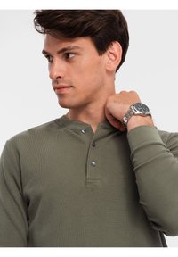 Olivgrünes Langarm-Henley-Shirt aus strukturiertem Stoff, mit einem geknöpften Ausschnitt und einem runden Hals.