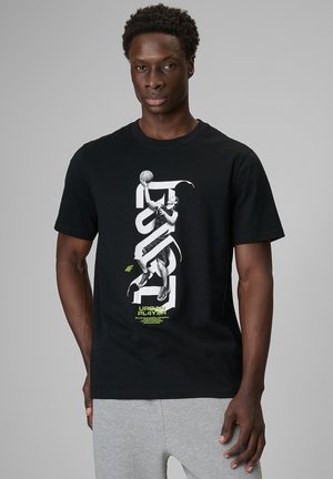 Mężczyzna w czarnej koszulce z grafiką koszykarza i napisem „Urban Player”, w połączeniu z jasno szarymi spodenkami dresowymi, na szarym tle.